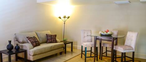Ett vardagsrum med en beige soffa, två sidobord, en golvlampa och ett matbord med stolar.