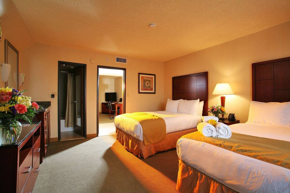 Een hotelkamer met twee bedden, een bureau met een bloevas, een lamp en een foto aan de muur.
