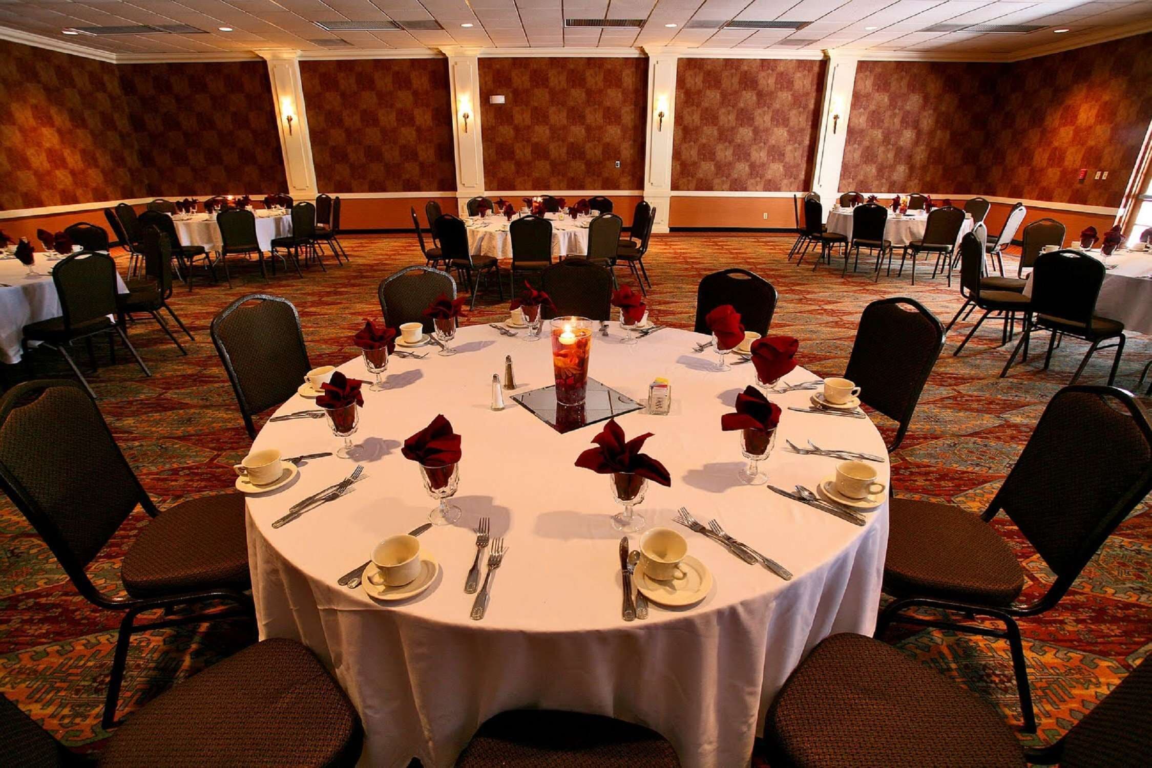 A banquet hall with round tables set for dining, featuring white tablecloths, red napkins, and candles.