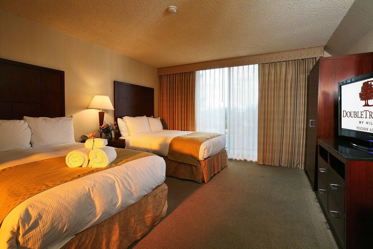 Een hotelkamer met twee bedden, een televisie en een groot raam met gordijnen.