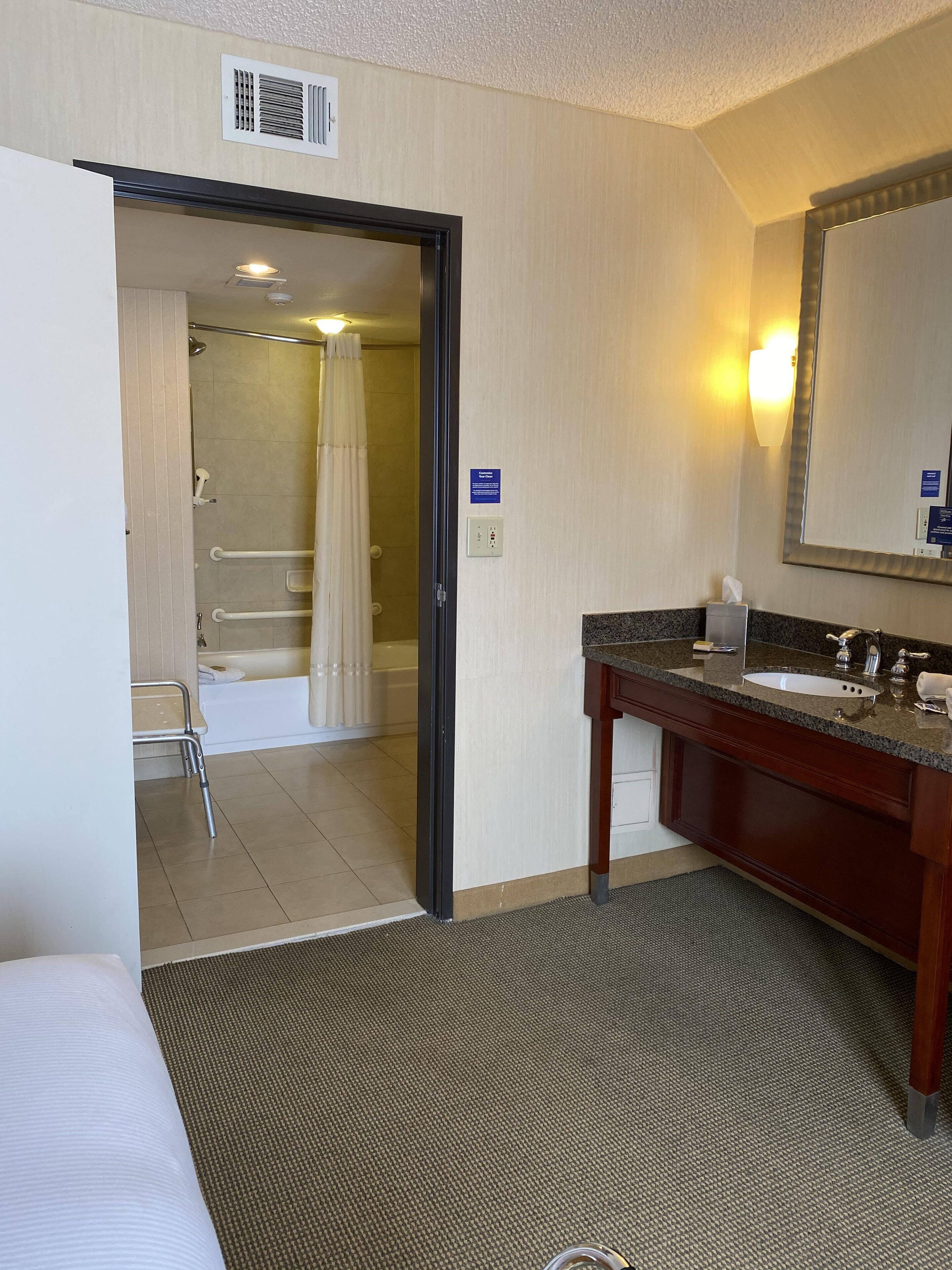 A hotel bathroom with a shower, a sink, and a mirror.