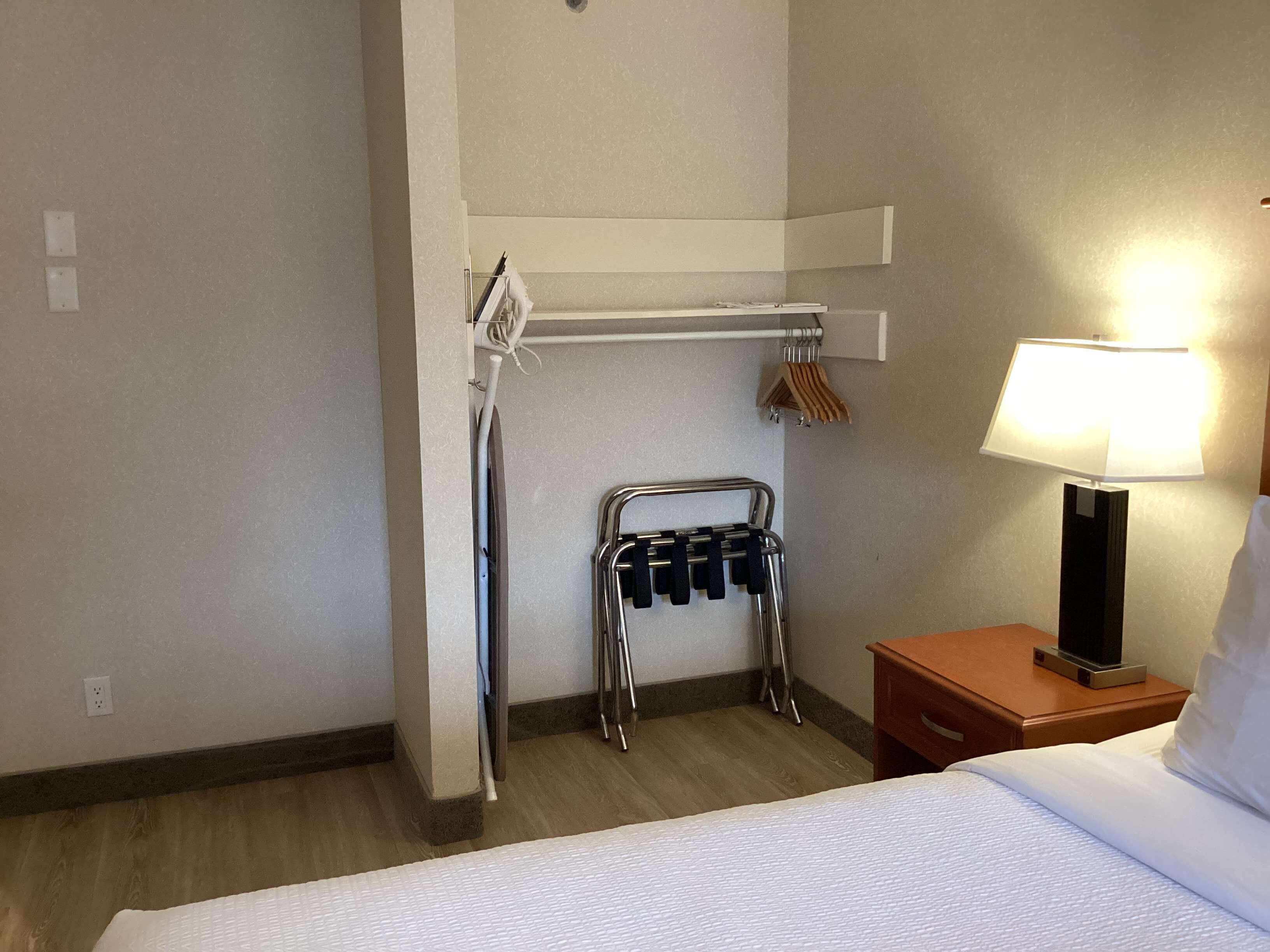 Ein Hotelzimmer mit Bett, Nachttischlampe, Kleiderhaken und Handtuchhalter.
