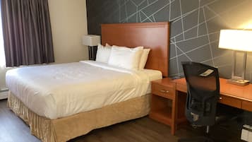 Ett hotellrum med en stor säng, ett skrivbord med en stol, en lampa och ett nattduksbord.