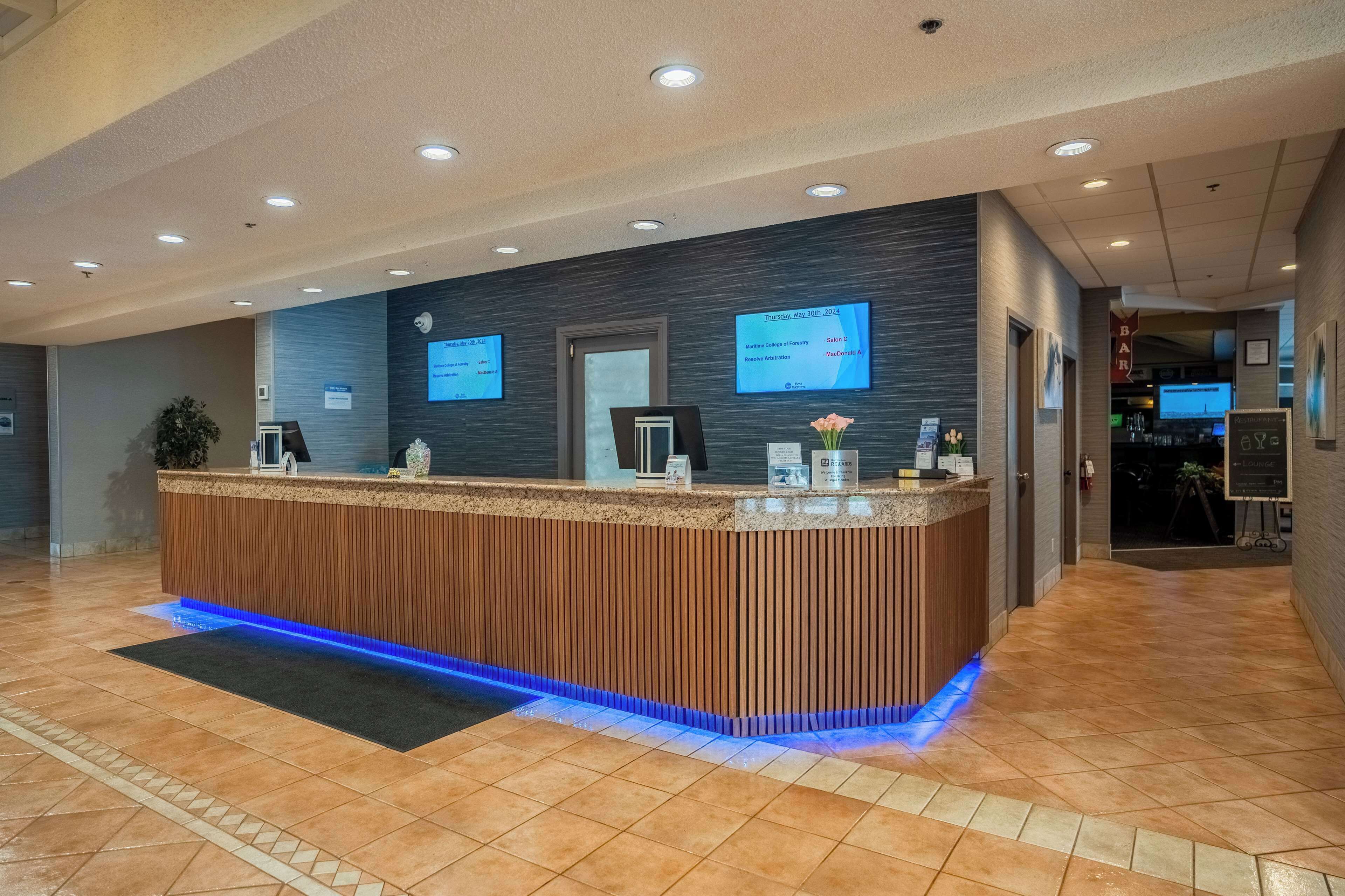 Una reception con finiture in legno e illuminazione blu a LED, affiancata da due schermi digitali che mostrano informazioni.