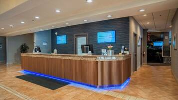 Una reception con finiture in legno e illuminazione blu a LED, affiancata da due schermi digitali che mostrano informazioni.