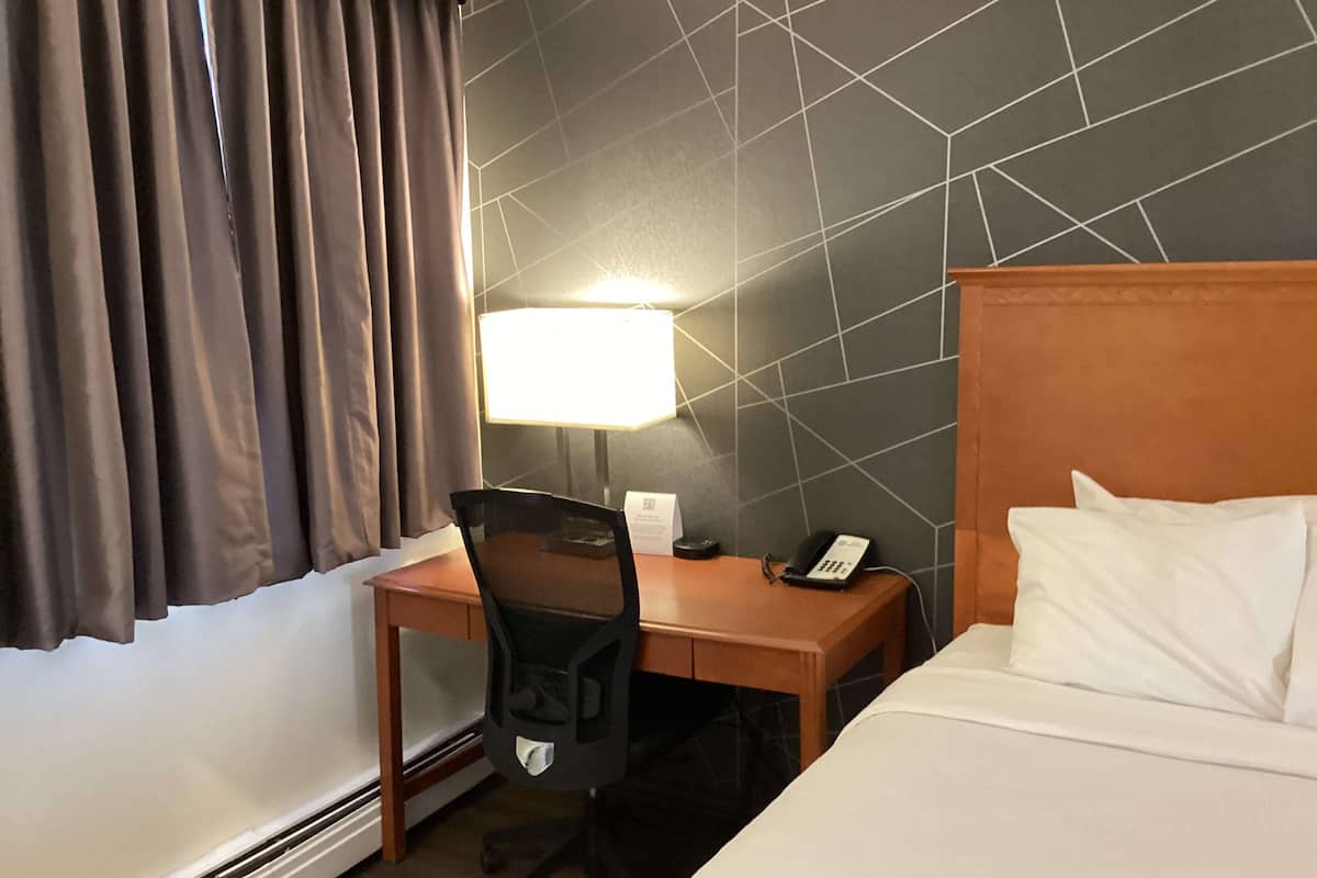 A hotel room with a bed, a desk with a chair, a telephone, and a lamp.