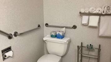 Een badkamer met een wit toilet, een handgreep, een handdoekrek met handdoeken en een plank met toiletartikelen.
