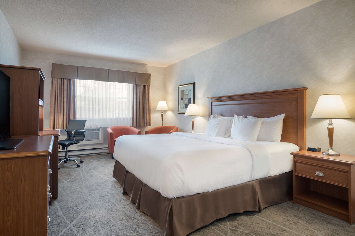 A hotel room with a large bed, two bedside tables with lamps, a desk with a chair, and a television.