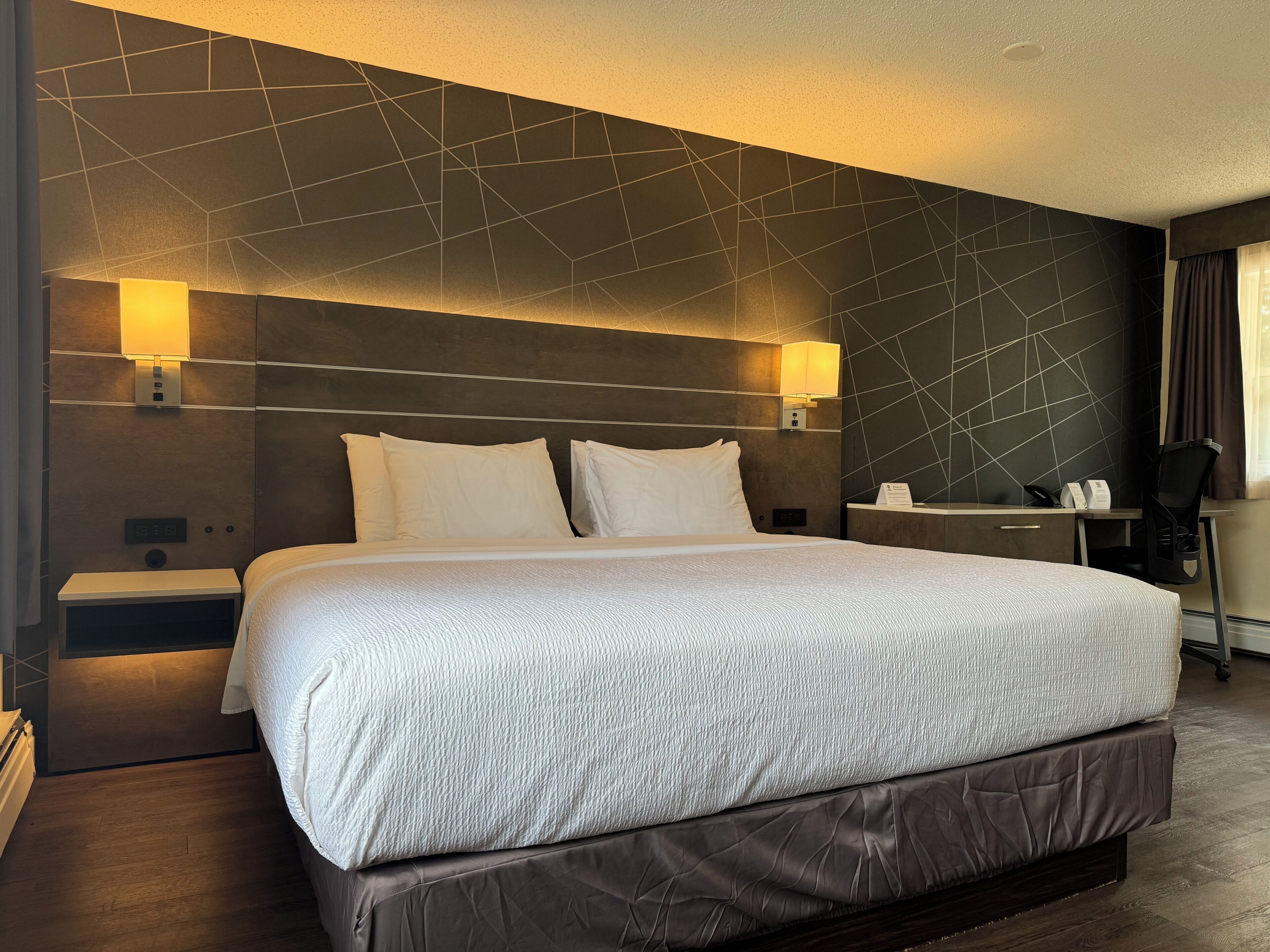 Una habitación de hotel moderna con una cama grande, dos lámparas de noche, un escritorio y una silla.