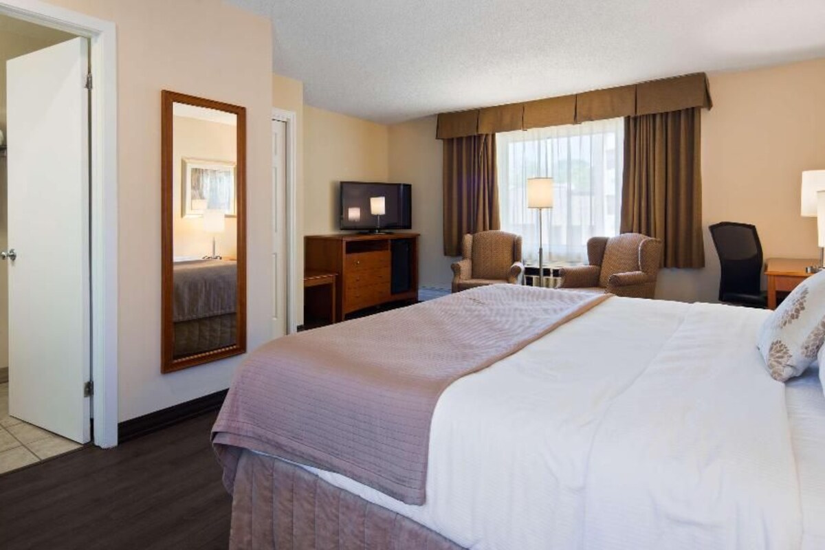 A hotel room with a large bed, a desk with a television, a chair, and a window with curtains.