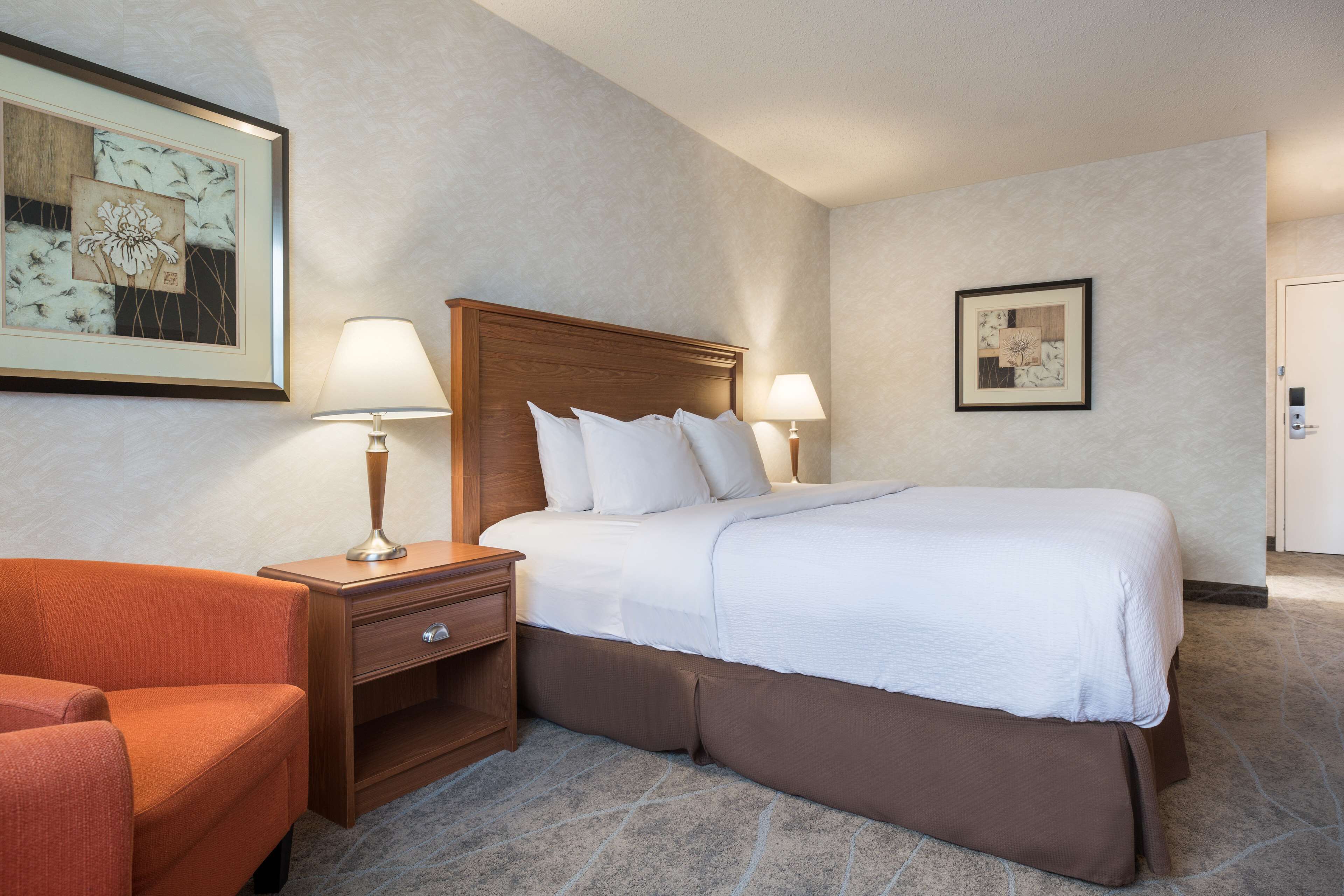 Una habitación de hotel con una cama grande, dos mesitas de noche con lámparas, una silla y obras de arte en las paredes.
