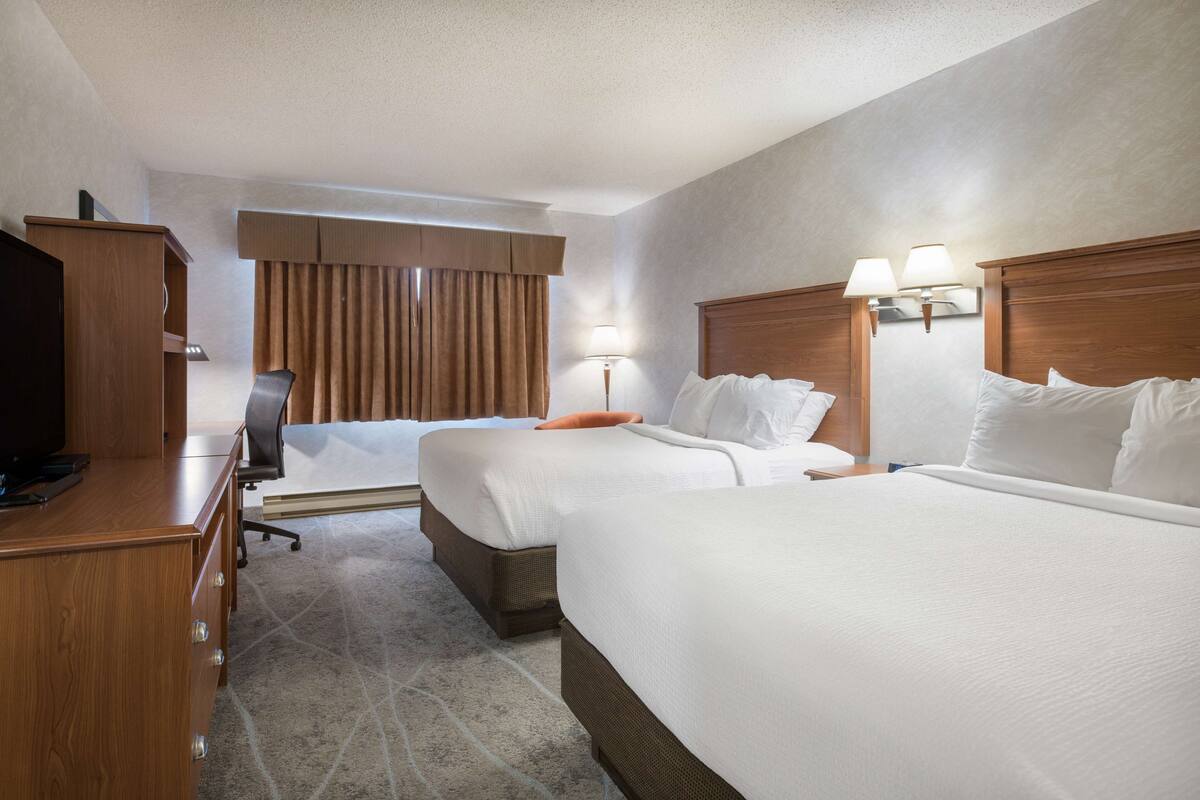 A hotel room with two beds, a desk, a television, and a window with curtains.