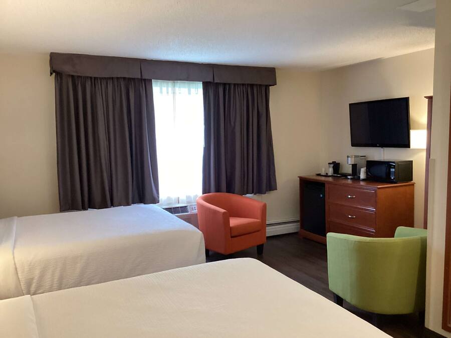 A hotel room with two beds, a television, a microwave, and a desk with a chair.