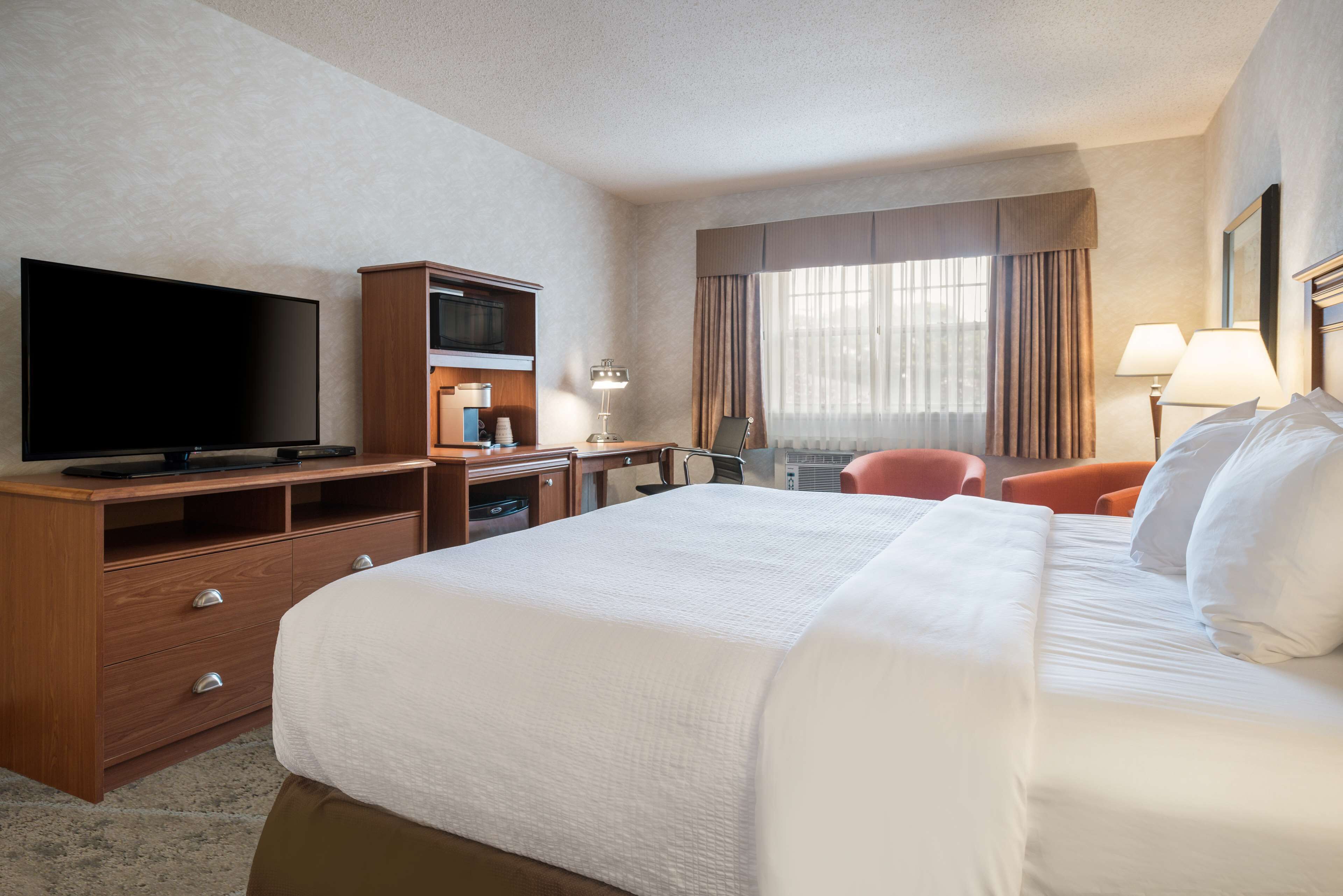 Habitación de hotel con una cama grande, televisión de pantalla plana, cómoda de madera, escritorio y una silla.