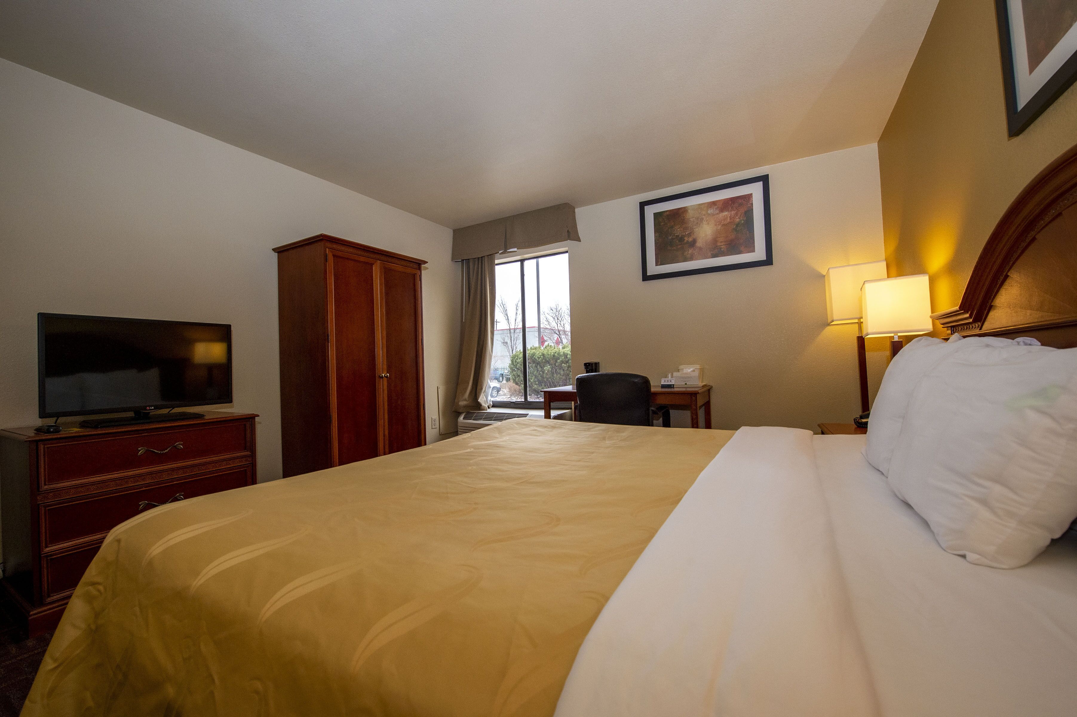 Habitación de hotel con una cama grande, un televisor en un aparador de madera, un escritorio con una silla y una ventana con vistas al exterior.