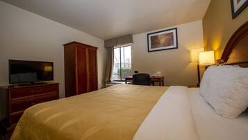Habitación de hotel con una cama grande, un televisor en un aparador de madera, un escritorio con una silla y una ventana con vistas al exterior.