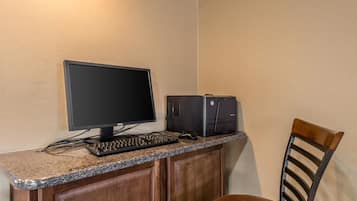 A computer desk with a monitor, keyboard, and printer, a chair, and wooden cabinets.