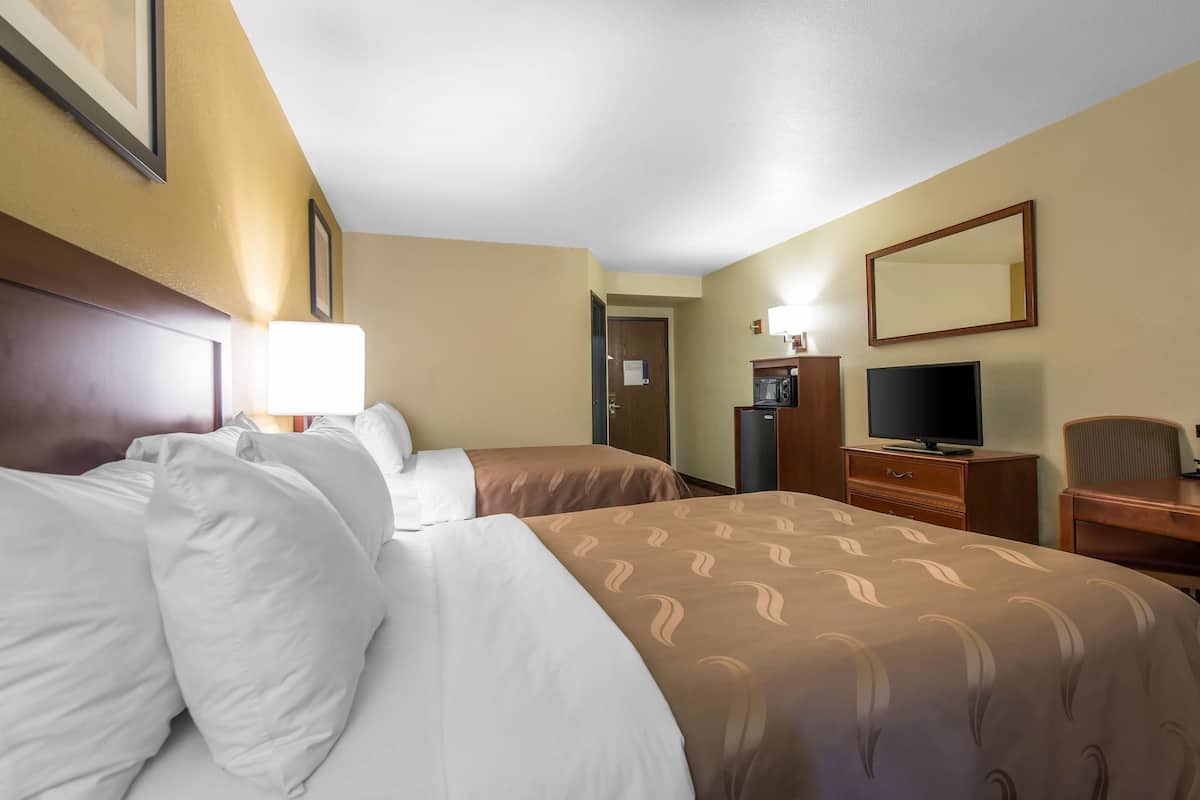 A hotel room with two beds, a television, a desk, and a mirror.