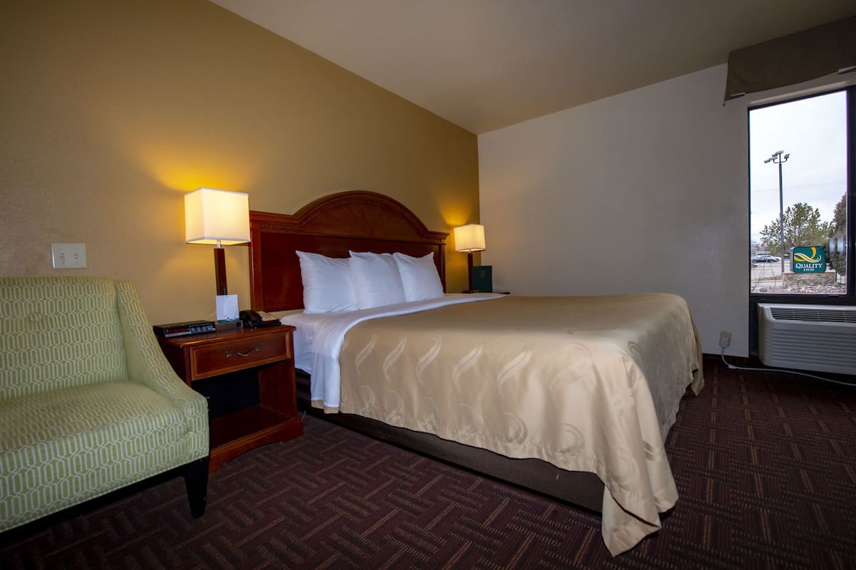 A hotel room with a bed, two bedside lamps, a nightstand, a chair, and a window with a view of the outside.