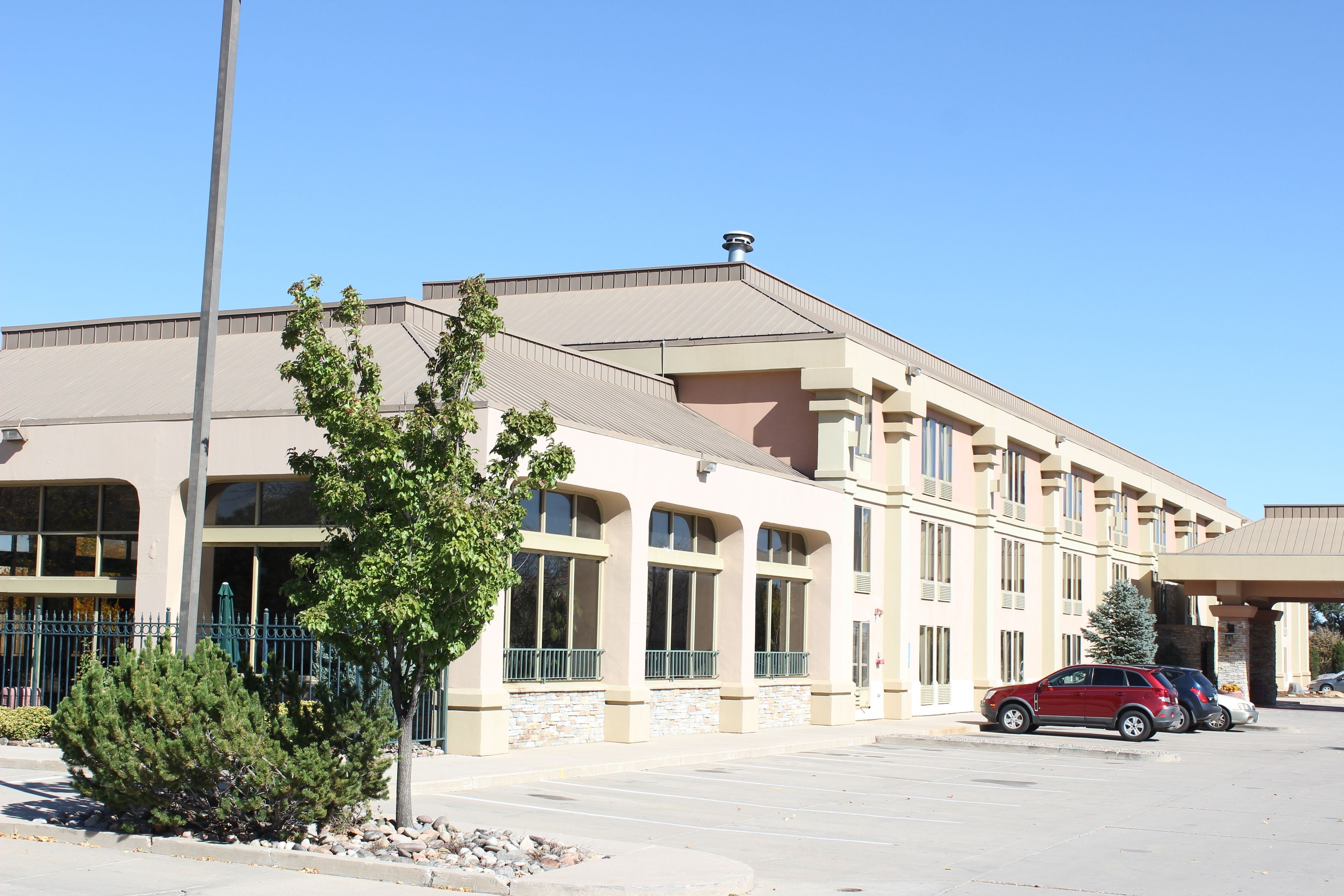 A multi-story hotel with a beige facade, large windows, and a parking lot with several cars.