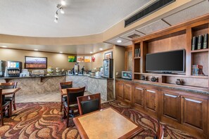 A hotel lobby with a dining area, kitchen, and a flat-screen TV.