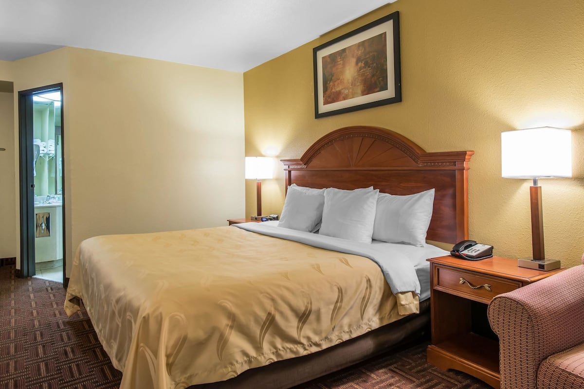A hotel room with a large bed, two bedside lamps, a nightstand with a phone, and a framed picture on the wall.