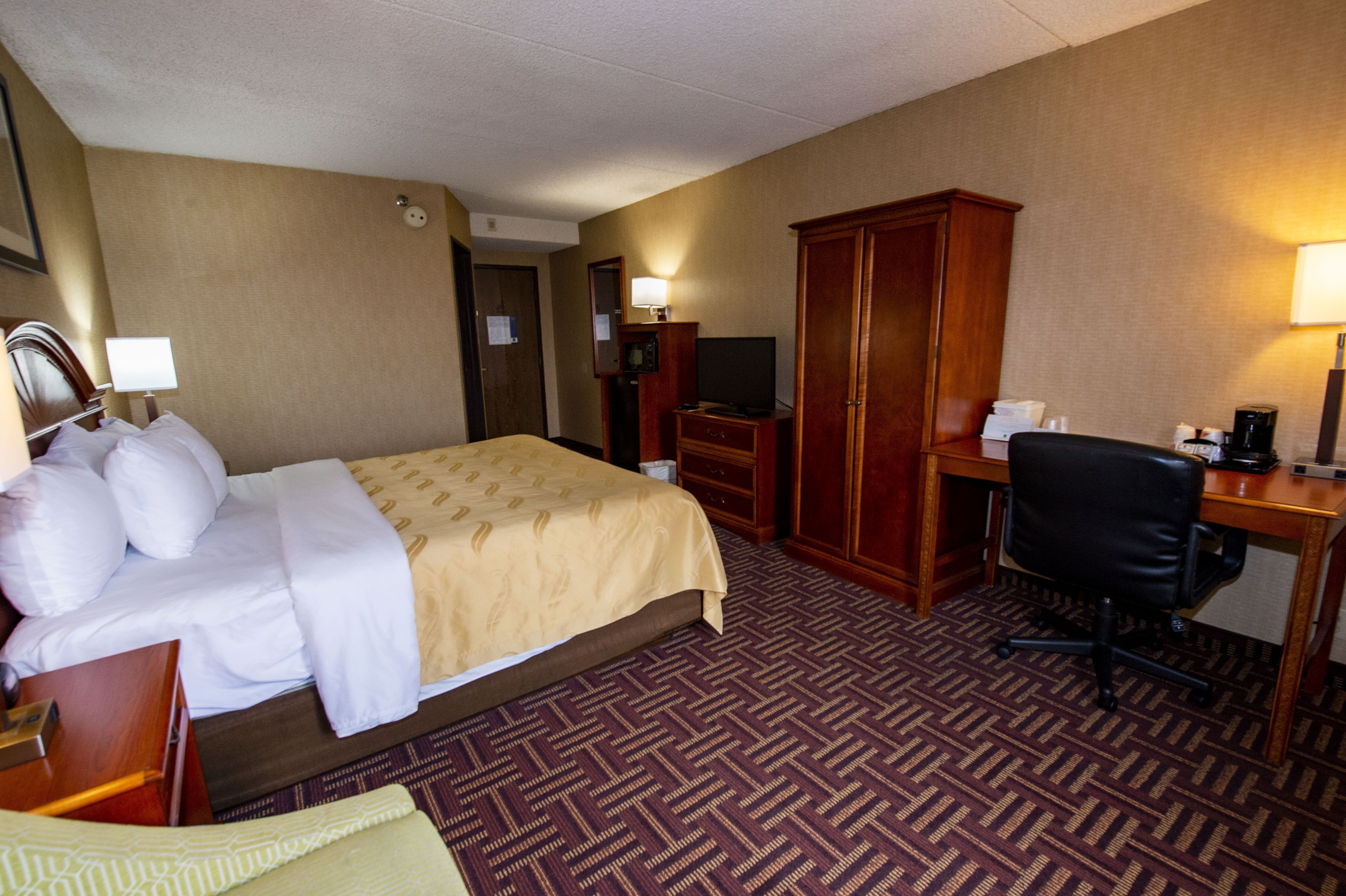 Una habitación de hotel con cama, escritorio, silla, armario y televisor.