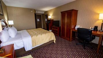 Una habitación de hotel con cama, escritorio, silla, armario y televisor.