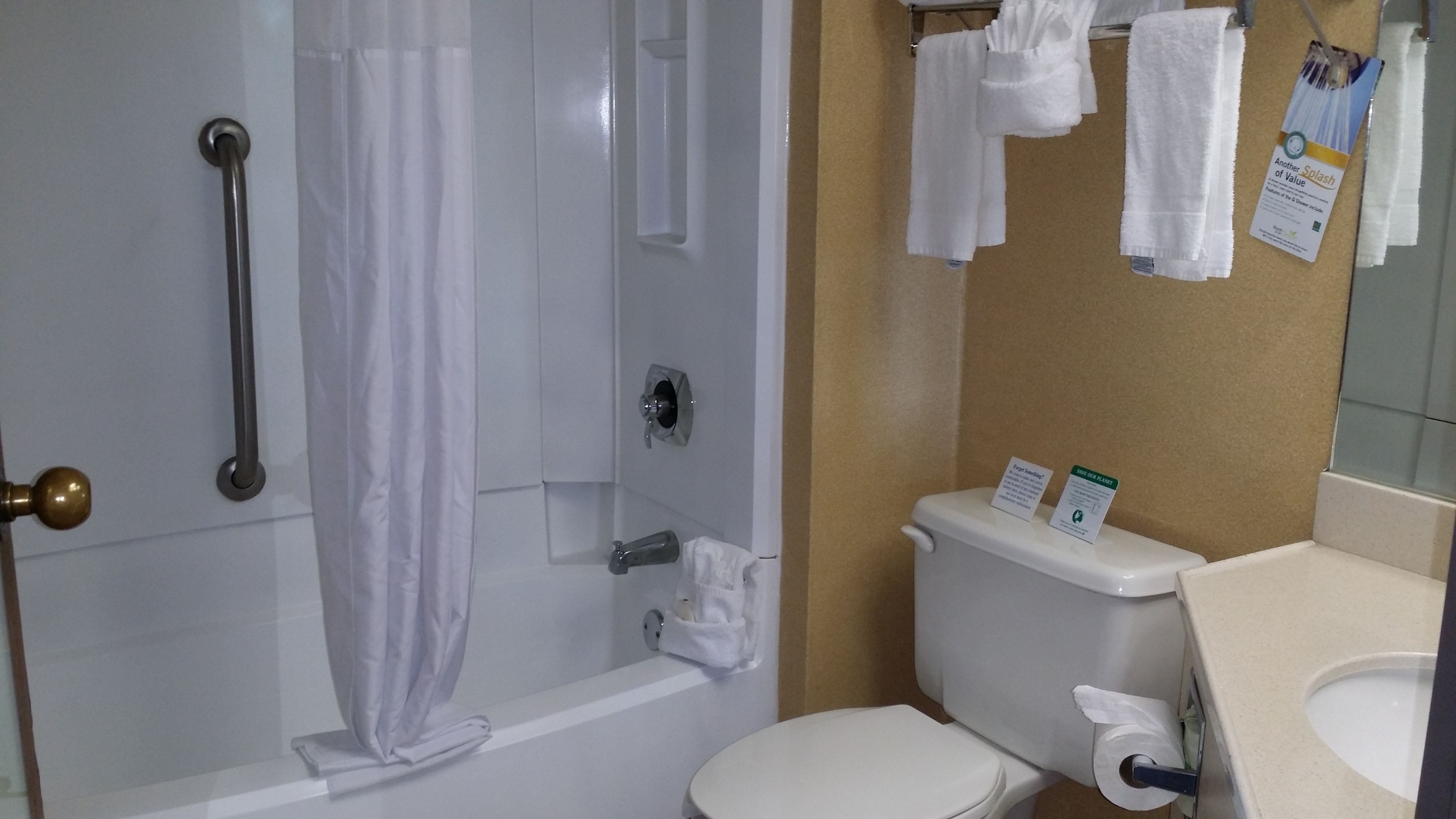 A bathroom with a bathtub, toilet, and a shower curtain. There are towels hanging on the wall and a sign about water conservation.