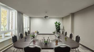 Ein Konferenzraum mit einem langen Tisch, Stühlen, einem Projektor und einer Topfpflanze.