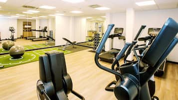 Un gimnasio con equipamiento de ejercicio, un espejo y una colchoneta verde.