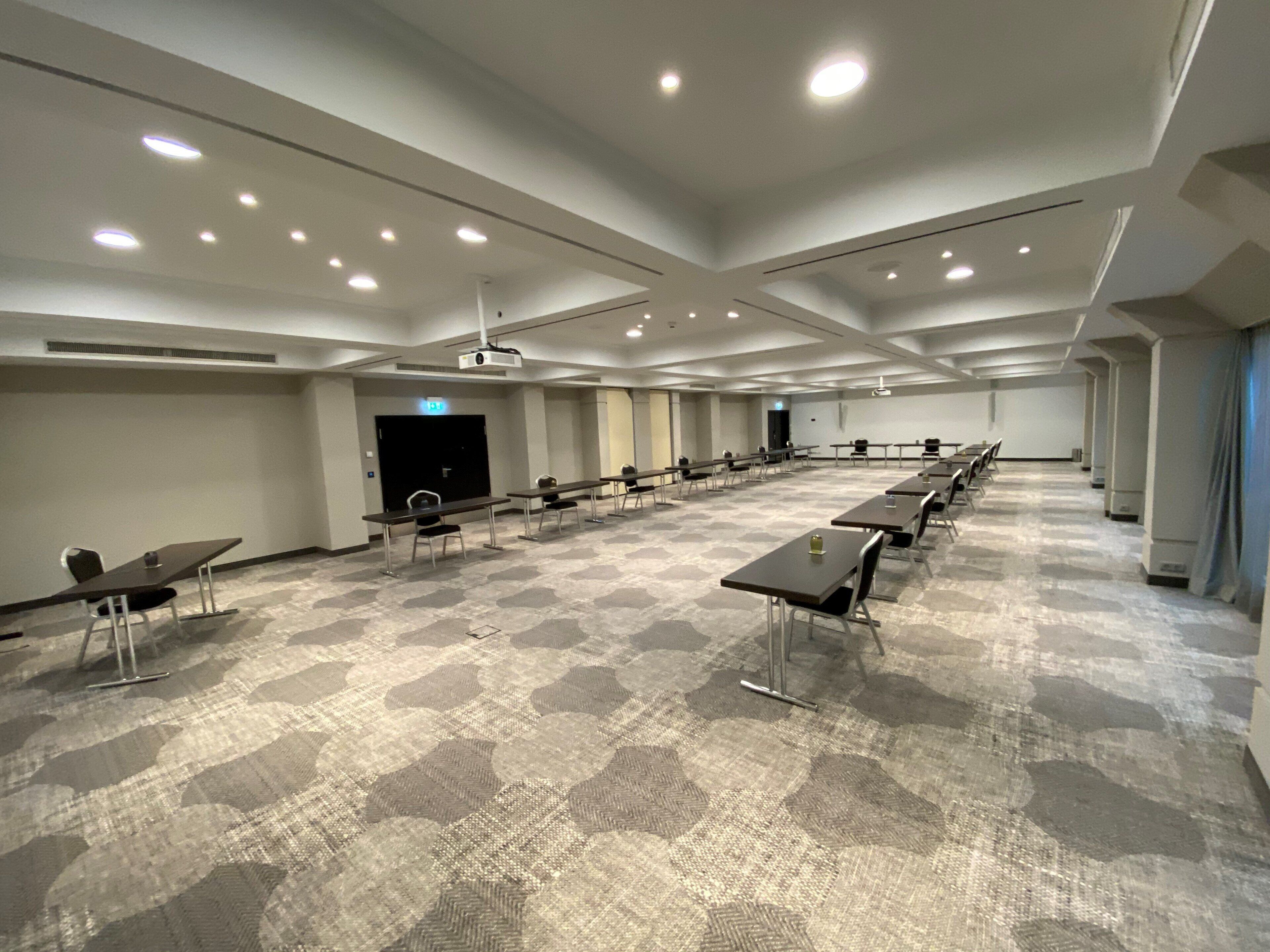 A conference room with tables and chairs, a projector, and a carpeted floor.