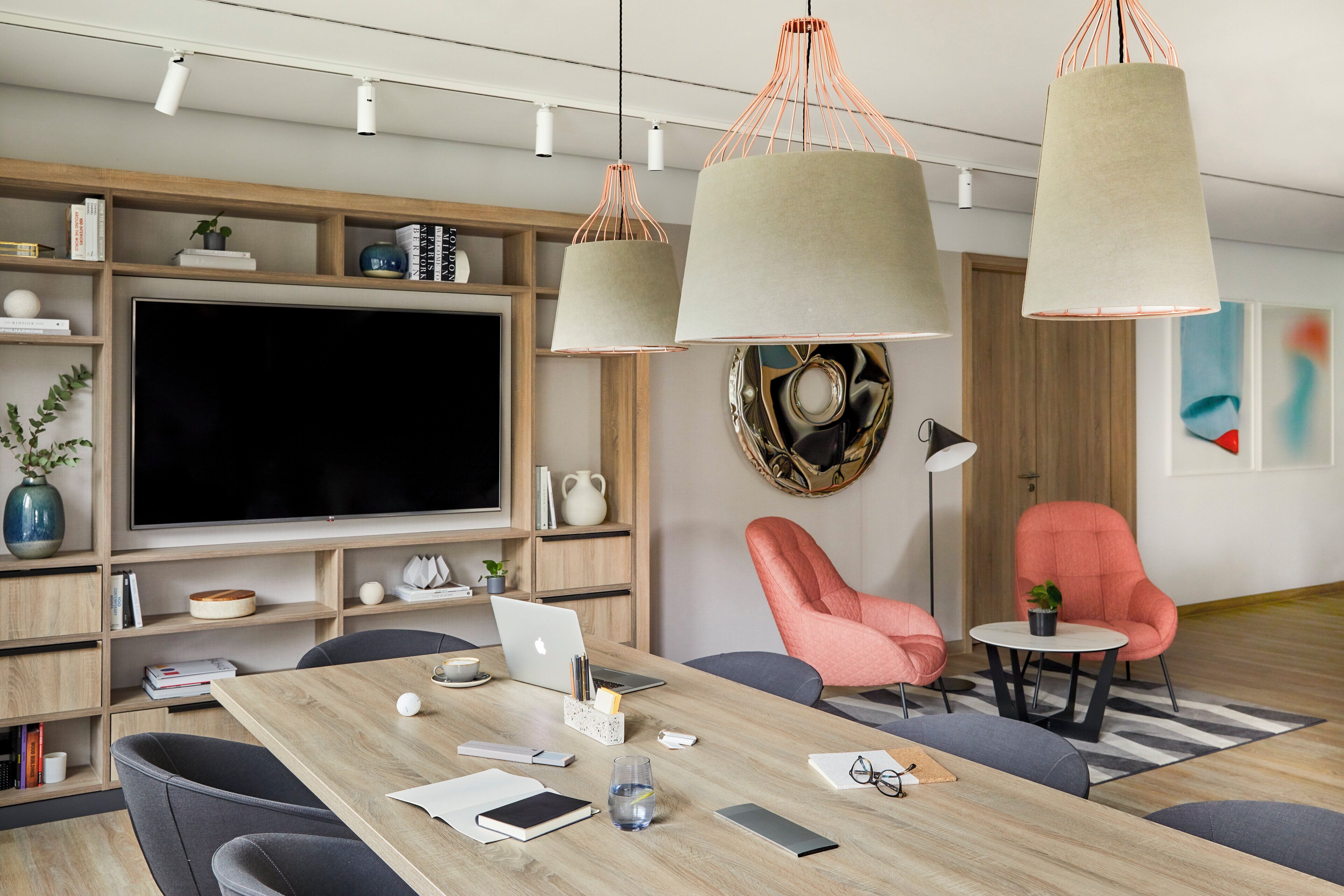 Una sala moderna con un televisor de pantalla plana grande, estanterías de madera, una mesa de comedor con sillas e iluminación colgante.
