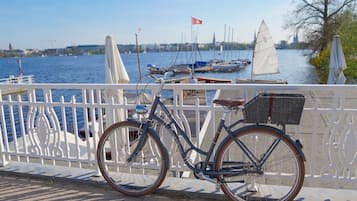 Una bicicleta estacionada frente a la orilla del agua, con una baranda blanca, y una vista del agua, además de veleros al fondo.