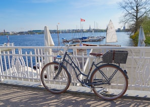 Una bicicleta estacionada frente a la orilla del agua, con una baranda blanca, y una vista del agua, además de veleros al fondo.