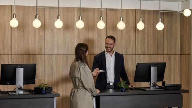 Un espace d’accueil avec des murs recouverts de panneaux en bois, deux comptoirs d’accueil et trois luminaires suspendus.