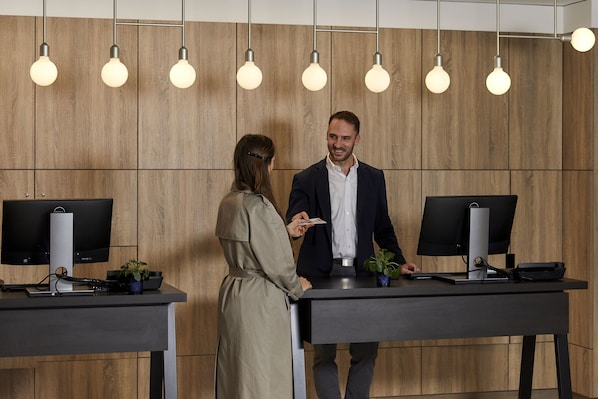 Un área de recepción con paneles de madera, dos mostradores de recepción y tres lámparas colgantes.