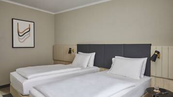 A hotel room with two beds, a bedside table with a glass of water, and a wall-mounted lamp.