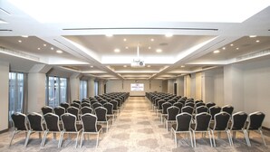 Une salle de conférence avec des rangées de chaises, un sol recouvert de moquette et un plafond doté d’un éclairage encastré.