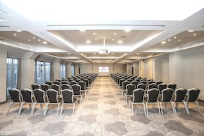 Un salón de conferencias con filas de sillas, piso alfombrado e iluminación empotrada en el techo.