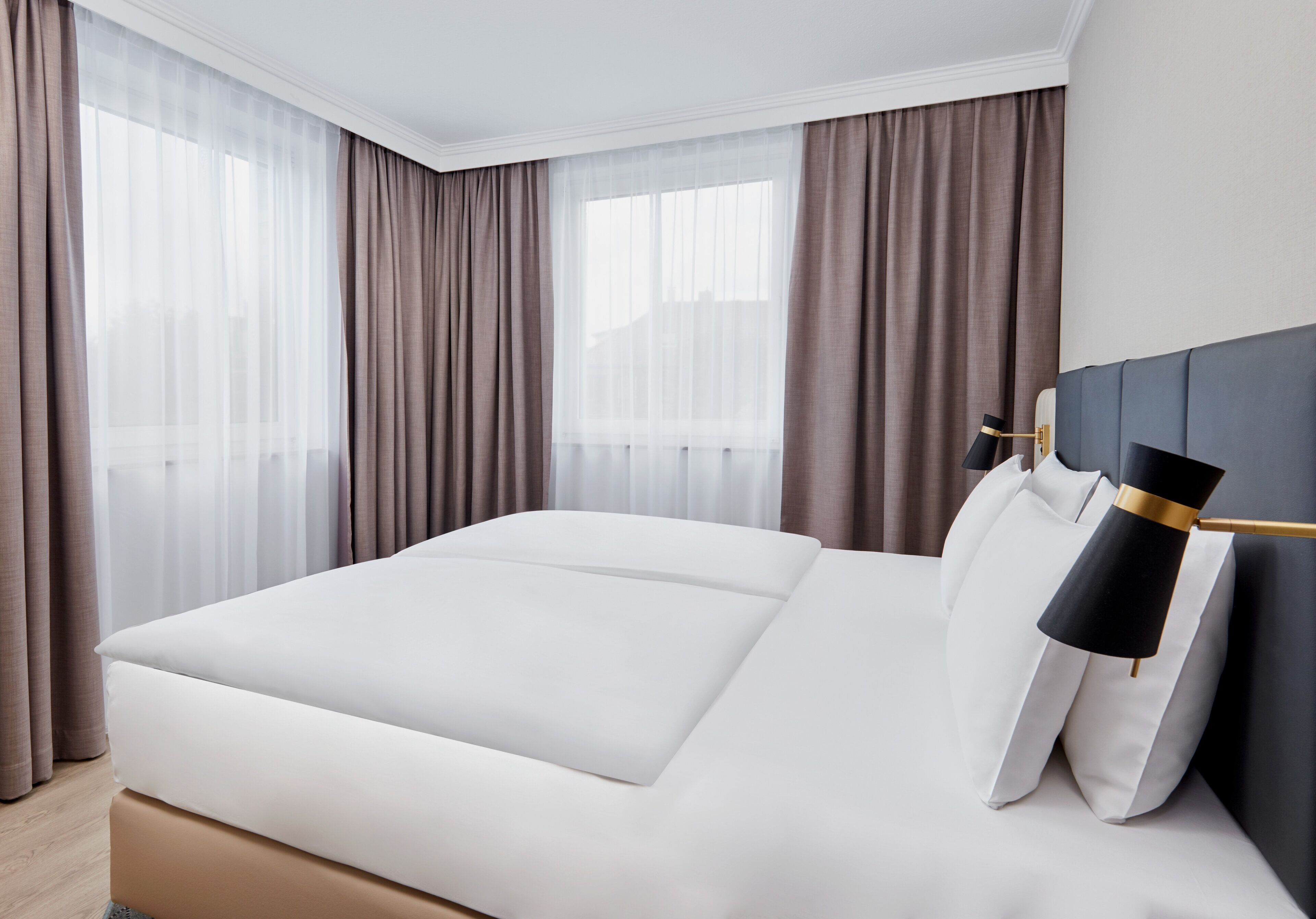 A modern hotel room with a large bed, a bedside table, and a lamp.