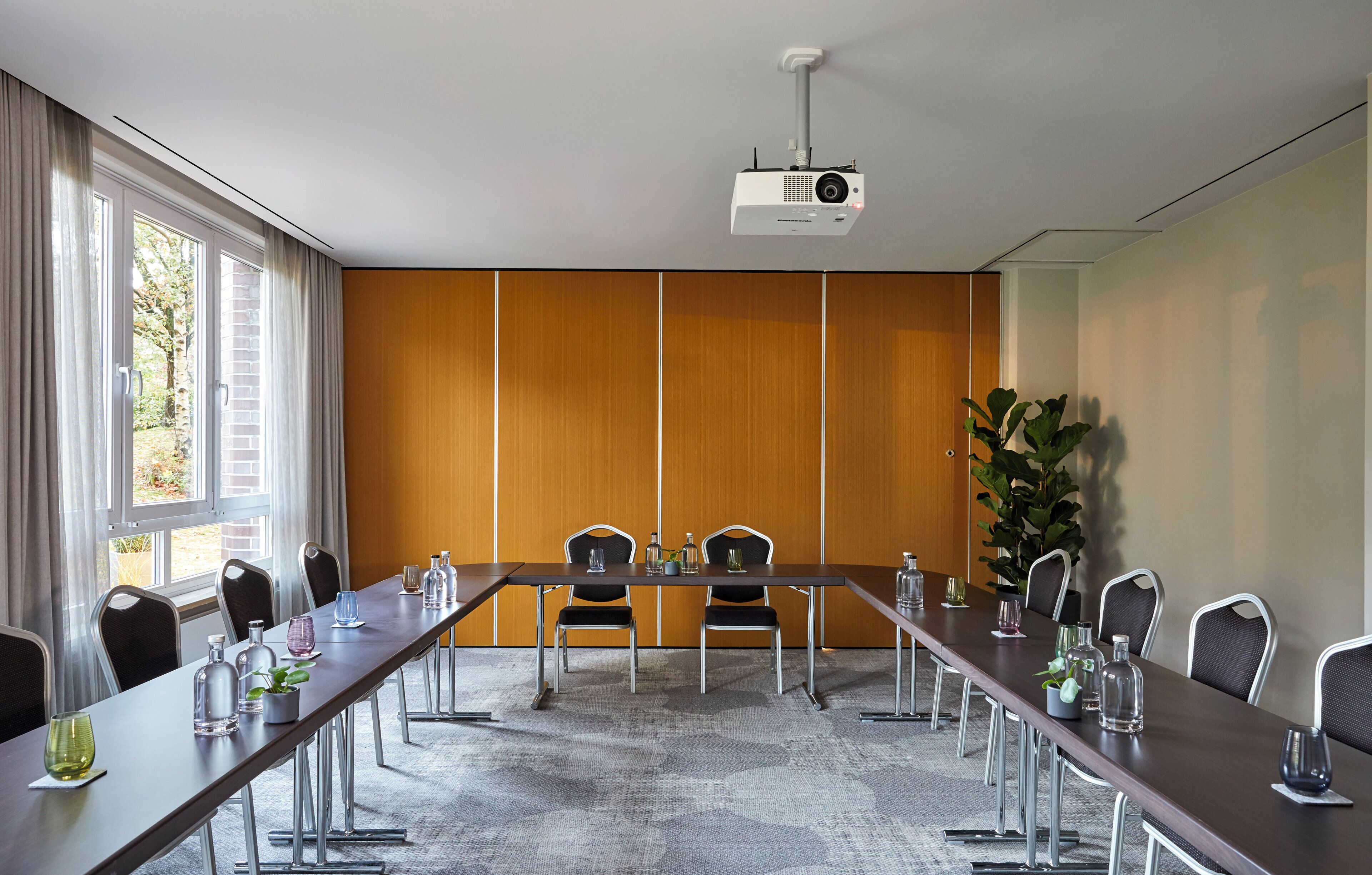 Une salle de conférence avec une longue table, des chaises, un projecteur et une grande plante.