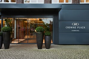 Exterior do Crowne Plaza Hamburgo com fachada moderna, grandes vasos de plantas e entrada de vidro transparente.