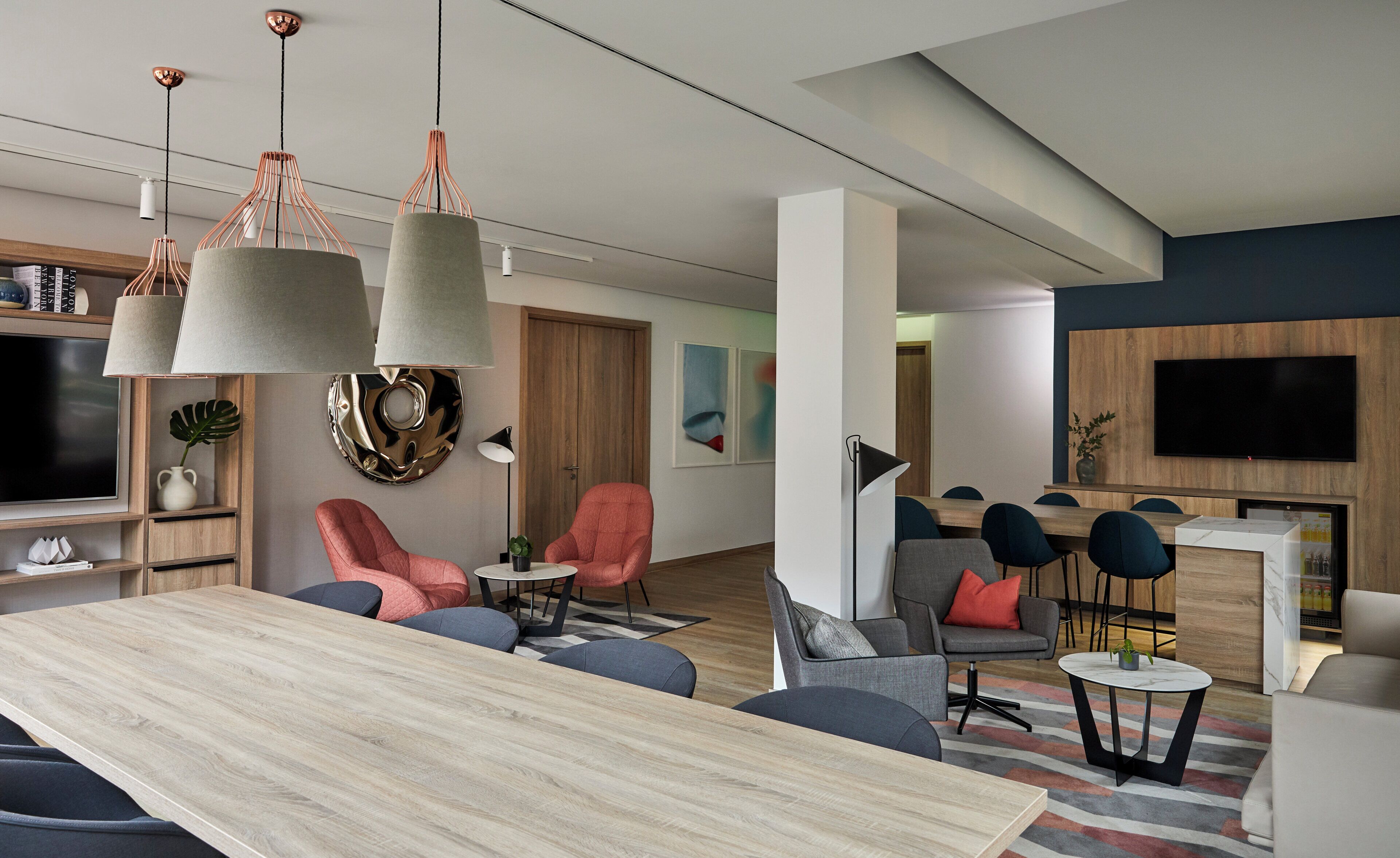 A modern living room with a wooden dining table, multiple seating options, and a flat-screen TV mounted on the wall.