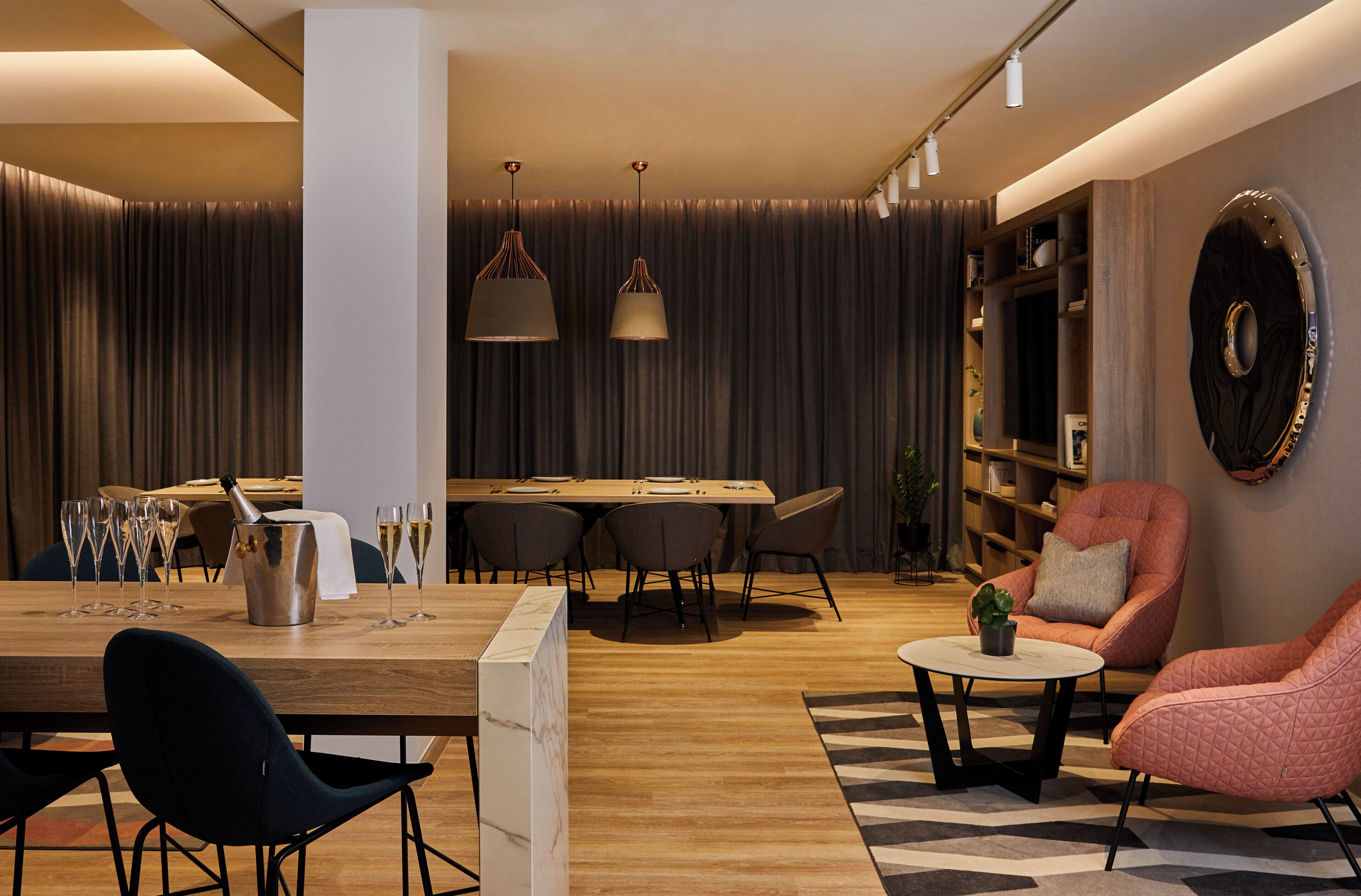 A modern living room with a wooden dining table, black and pink chairs, a coffee table, and a bookshelf.