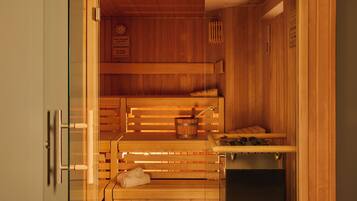 A sauna with wooden benches, a bench with a towel, a bucket with a brush, and a heater.
