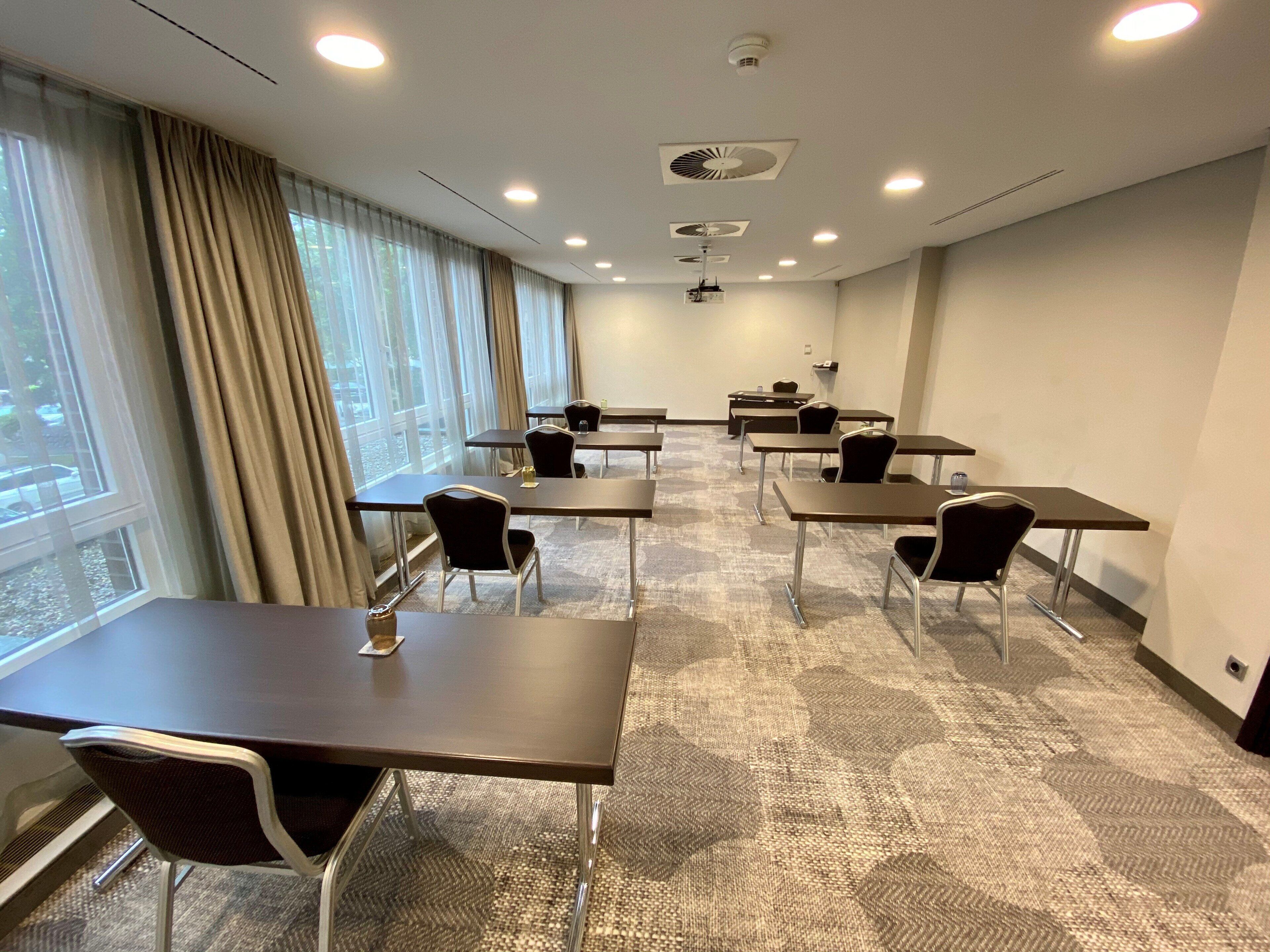 A conference room with tables and chairs, large windows with curtains, and ceiling lights.