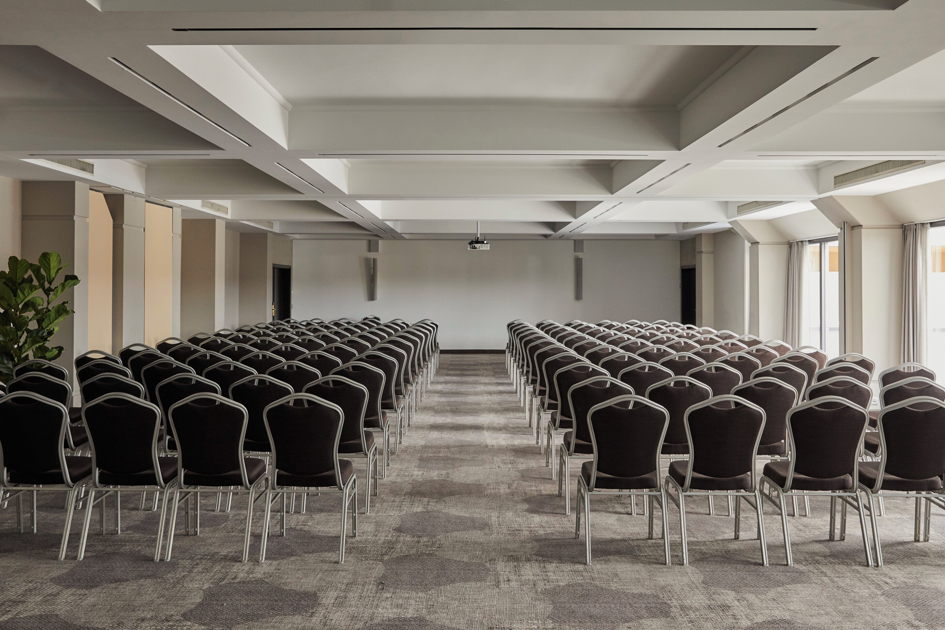 A conference room with rows of chairs, a carpeted floor, and a white ceiling with recessed lighting.