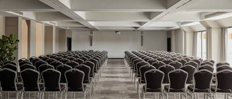 A conference room with rows of chairs, a carpeted floor, and a white ceiling with recessed lighting.