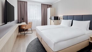 Une chambre d’hôtel moderne dotée d’un grand lit, d’un bureau avec une chaise, d’une télévision à écran plat et d’une armoire.